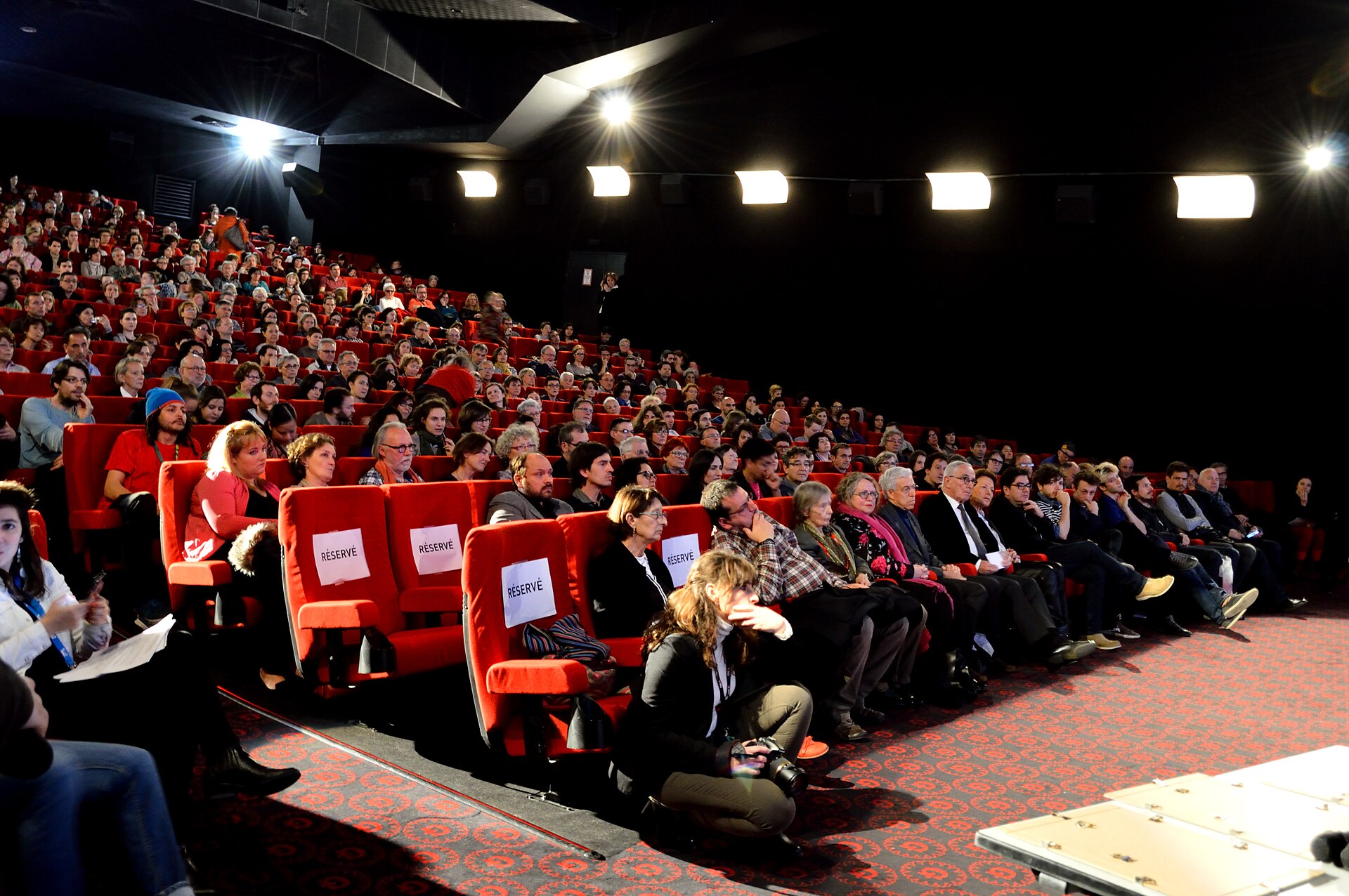Public installé dans une salle aux fauteuils rouges avant une projection